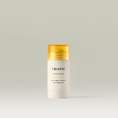 Tropic Sun Stick with green algae, vitamin E, and tamanu oil in a sleek white tube with a yellow cap, displayed on a neutral background.